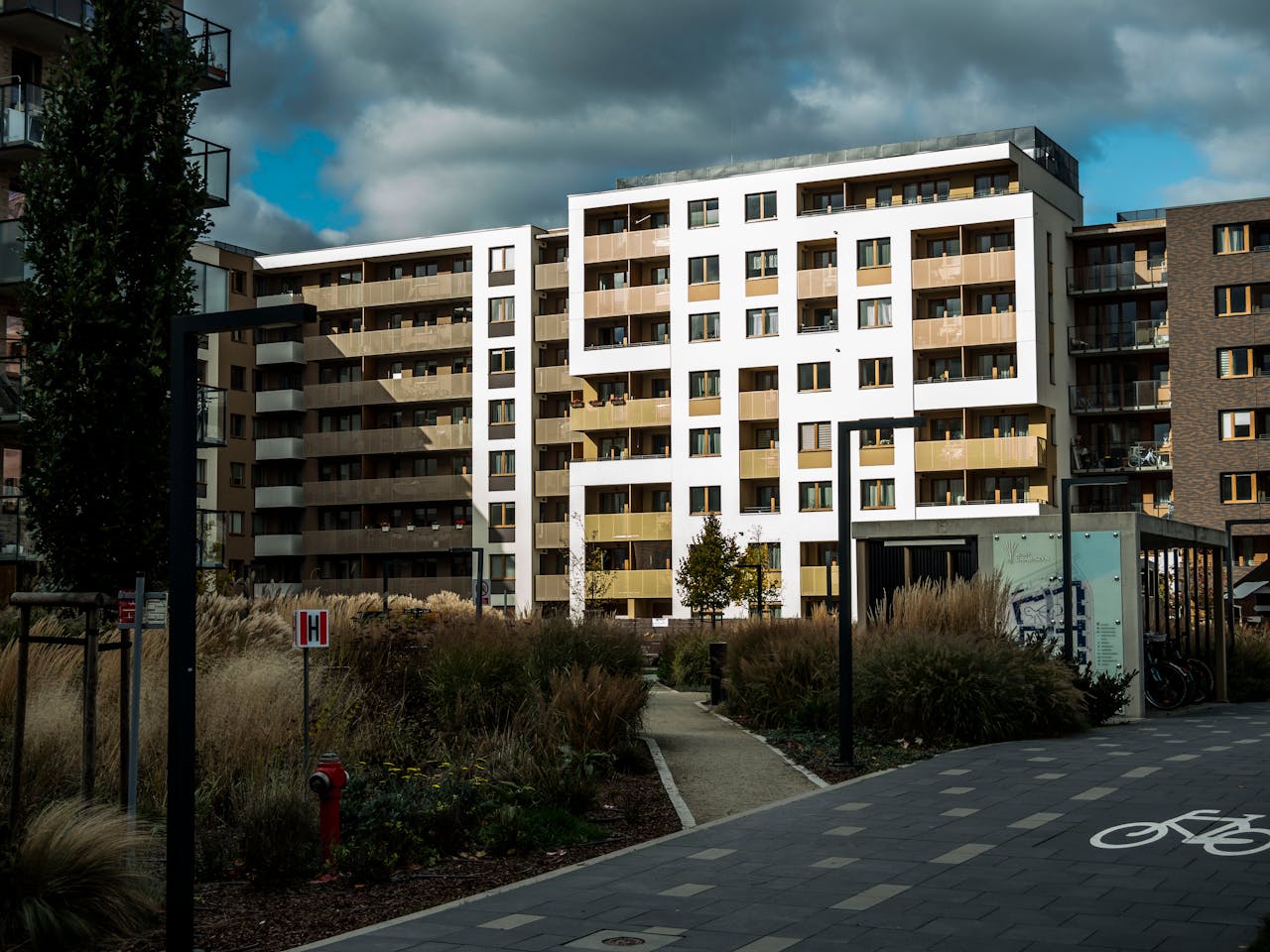 Contemporary apartment buildings surrounded by landscaped gardens and pathways under a cloudy sky.